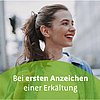 Person mit zurückgebundenem Haar in Jeansjacke und weißem Shirt vor urbanem Hintergrund mit Text „Bei ersten Anzeichen einer Erkältung“