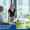 Drei Personen im Gespräch, zwei sitzen, eine steht – alle Gesichter sind unscharf dargestellt. Im Vordergrund befinden sich zwei Packungen des pflanzlichen Erkältungsmittels Imupret® N von Bionorica: Dragees und Tropfen. Text im Bild: „Wenn man nichts verpassen darf...“