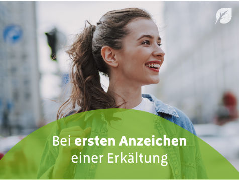 Person mit zurückgebundenem Haar in Jeansjacke und weißem Shirt vor urbanem Hintergrund mit Text „Bei ersten Anzeichen einer Erkältung“