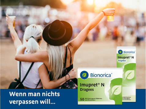 Zwei Personen mit erhobenen Armen und Getränken in der Hand auf einem Festival oder Outdoor-Event, von hinten fotografiert. Im Vordergrund sind zwei Packungen des pflanzlichen Erkältungsmittels Imupret® N von Bionorica zu sehen: Dragees (50 Stück) und Tropfen. Text im Bild: „Wenn man nichts verpassen will...“