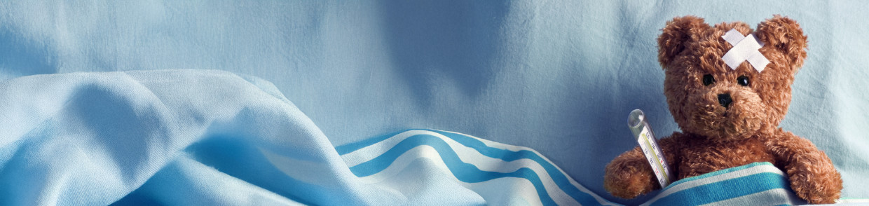 Ein brauner Teddybär liegt krank im Bett, mit einem weißen Pflaster in X-Form auf der Stirn. Er ist mit einer blau-weiß gestreiften Decke zugedeckt und hält ein Thermometer in der Pfote. Der blaue Hintergrund vermittelt eine ruhige Atmosphäre – die Szene symbolisiert Krankheit, Fürsorge und kindliches Trostbedürfnis.